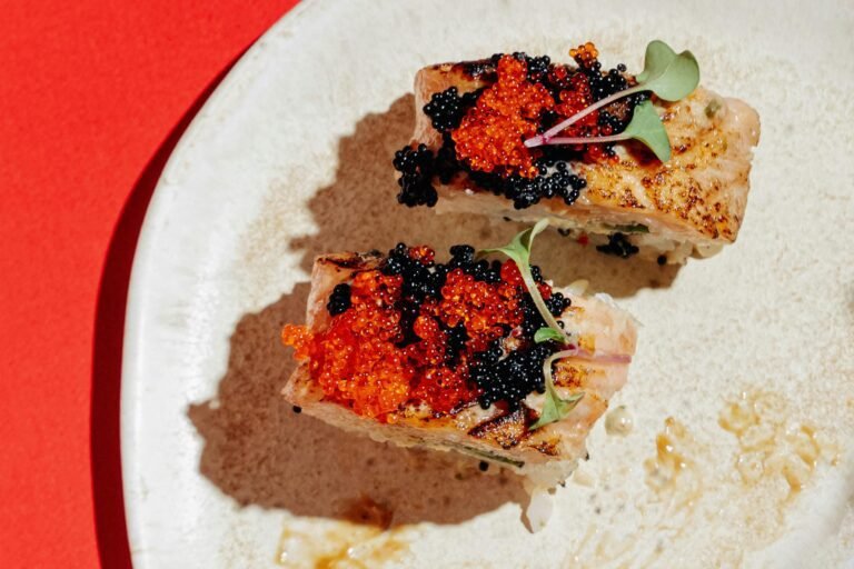 Delicious sushi pieces topped with red and black caviar served on a white plate.