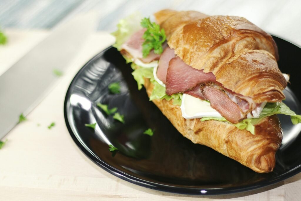 Tasty croissant sandwich with ham, cheese, and vegetables on a black plate.