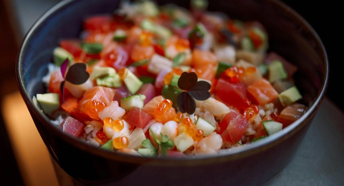 A colorful poke bowl featuring fresh salmon, avocado, and rice, topped with fish roe.