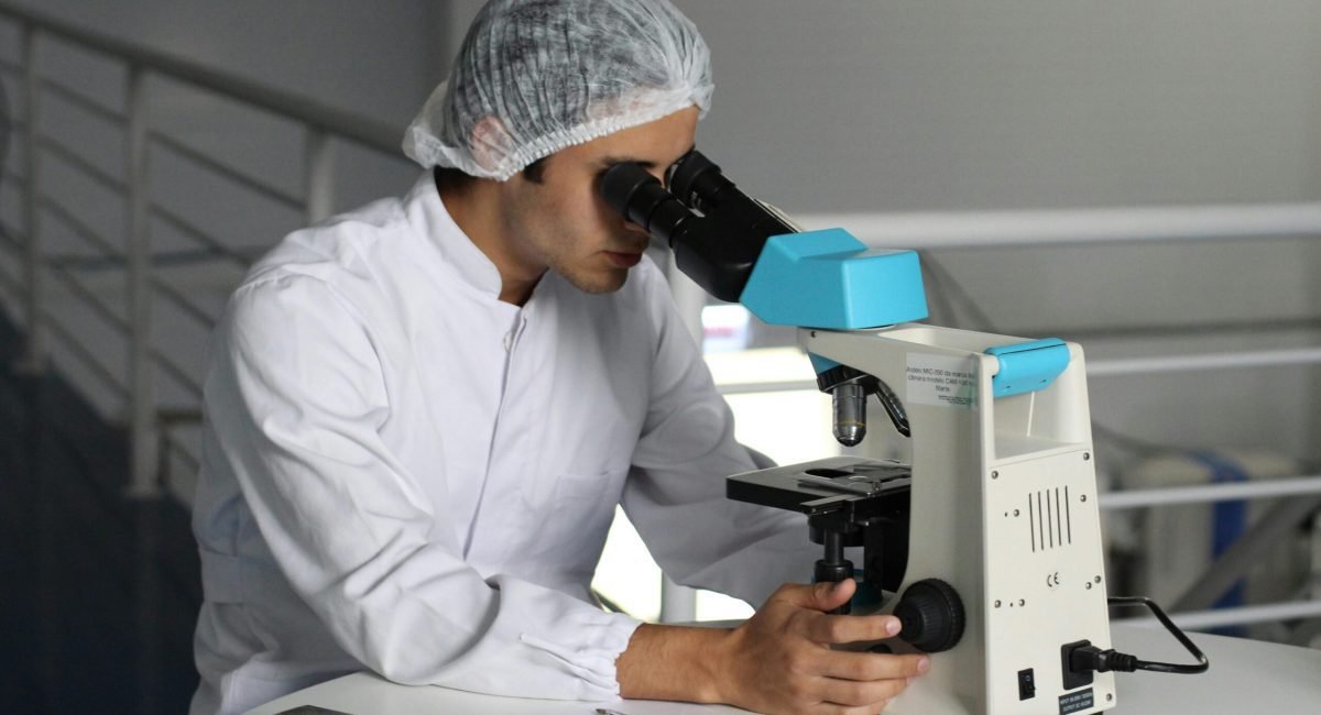 Scientist in a lab coat using a microscope to conduct research, focusing on healthcare improvements.