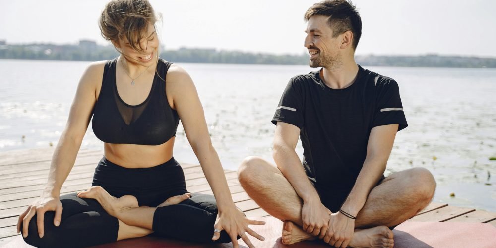 A man and woman practicing yoga and mindfulness on a lakeside pier on a sunny day.