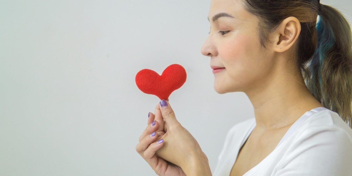 Side view of a young woman holding a red heart symbol, promoting love and wellness.